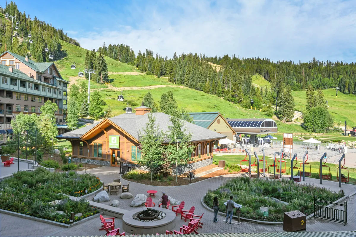 An inviting lodge exterior with outdoor seating, beautifully landscaped gardens, and a stunning mountain backdrop. The setting suggests a welcoming hub for gathering before or after a day of adventure, and hints at social, relaxing moments in nature.