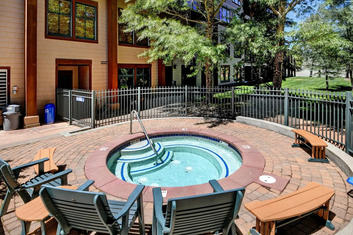 An inviting outdoor hot tub is surrounded by comfortable seating and lush greenery, set against the backdrop of a spectacular mountain vista. The scene captures guests relaxing in the hot tub, sharing laughter as the sun sets over the slopes, encapsulating the essence of post-adventure rejuvenation and luxurious relaxation.