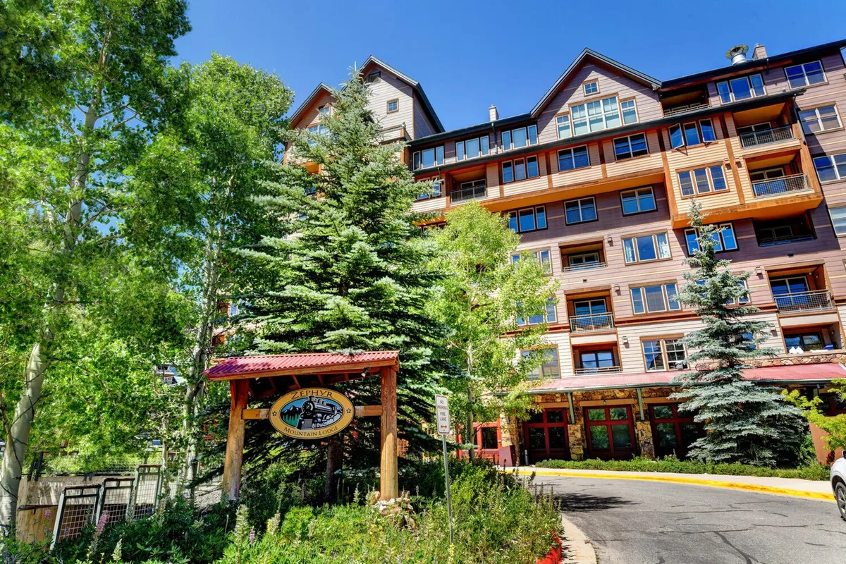 An inviting daytime exterior shot of the building's entrance, surrounded by trees and natural landscaping. Guests are seen walking, exploring the grounds, and enjoying the peaceful mountain setting, suggesting active engagement with nature and the outdoors.