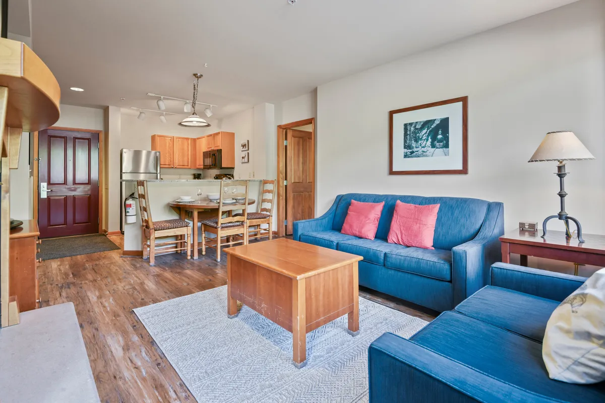 A cozy, inviting interior living space featuring a blue sofa, wooden coffee table, and visible dining and kitchen area. The setup is ideal for relaxed family evenings, playing board games, or unwinding together after a day of adventure.