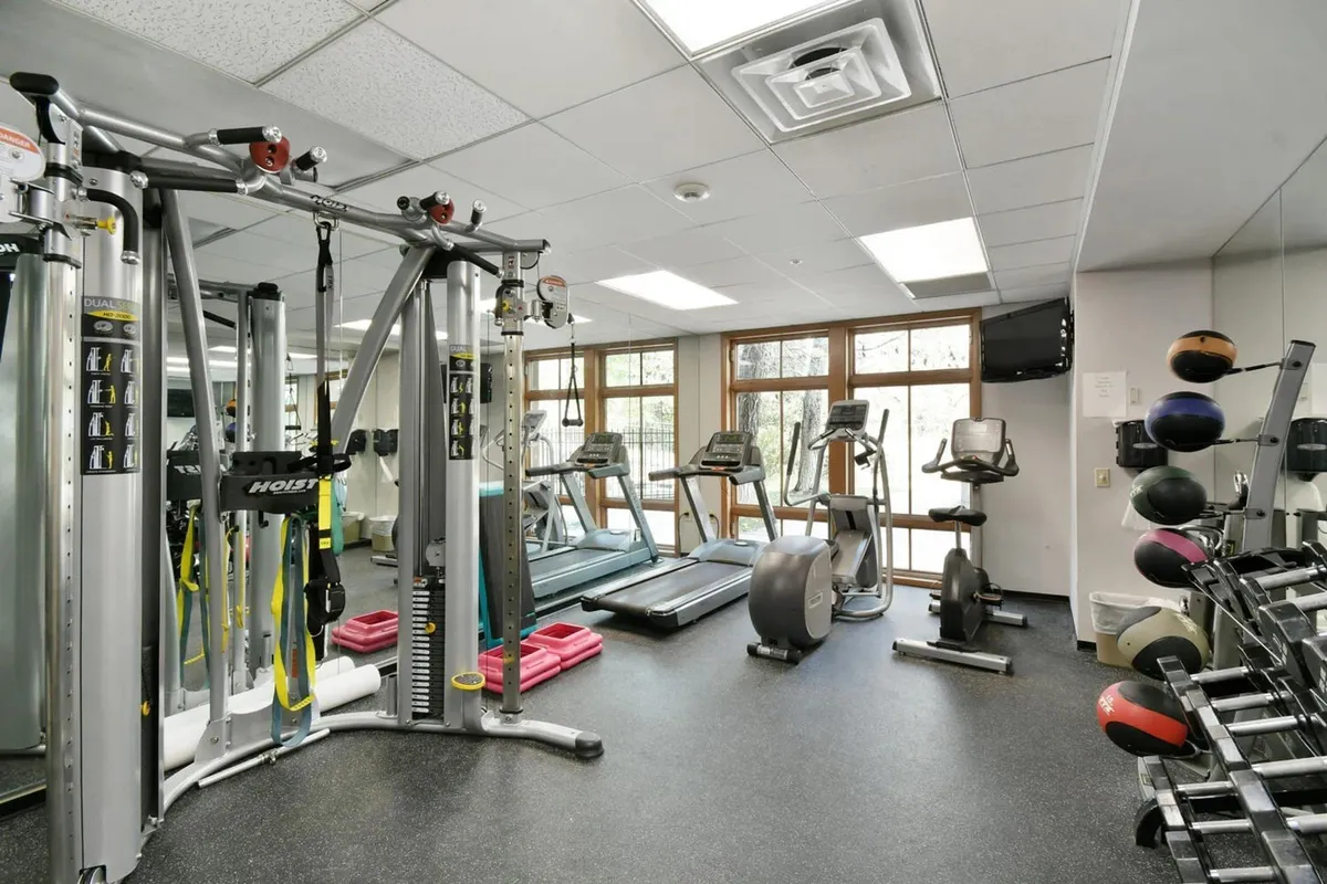 A bright, modern gym filled with multi-gym equipment, treadmills, and exercise balls. Large windows let in natural light and offer glimpses of the outdoors, while the space is designed to foster both solo workouts and group fitness classes.