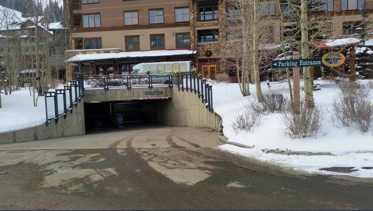 The entrance to the secure underground parking garage, framed by the building’s facade and surrounded by winter snow. The area is clearly marked for guests arriving by vehicle, with a sense of safety and accessibility.