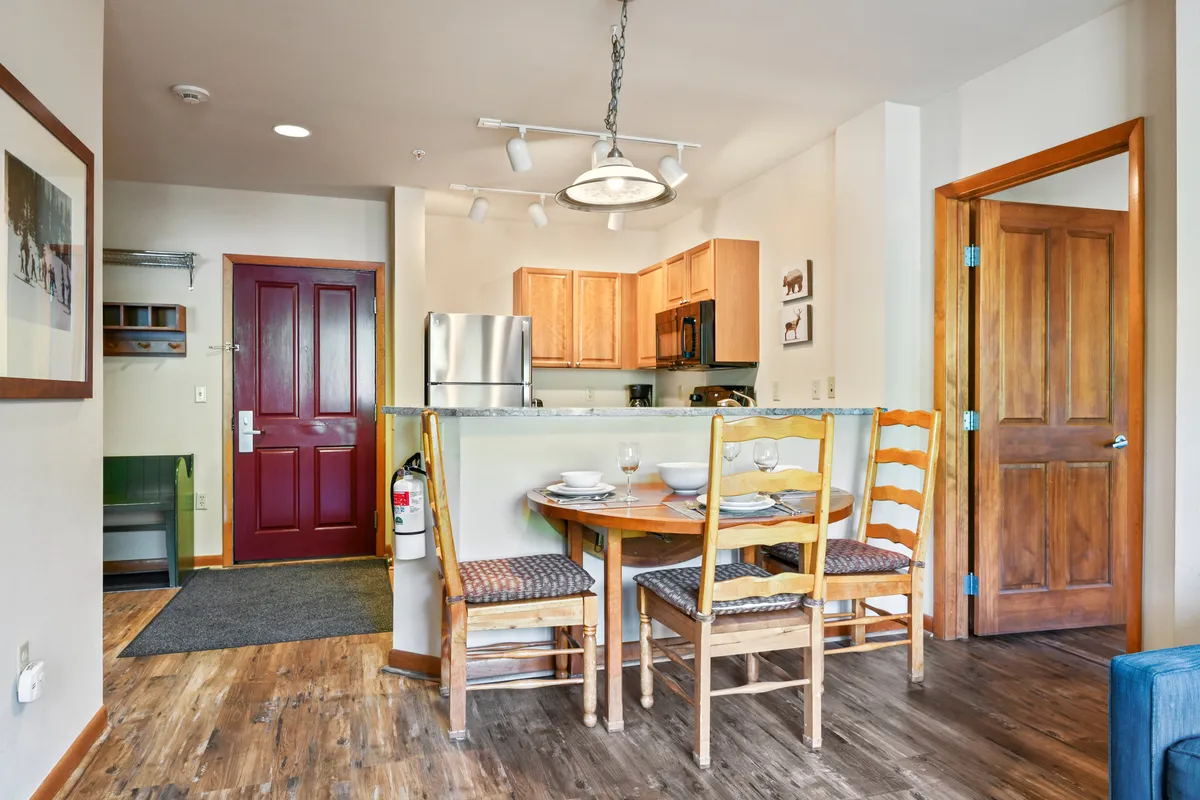 A wide view of the open-plan kitchen and dining area reveals a spacious cooking zone, a sturdy dining table with ample seating, and a distinctive red door. The layout shows clear sightlines for socializing, making it easy to move between preparing food and gathering for meals or special occasions.